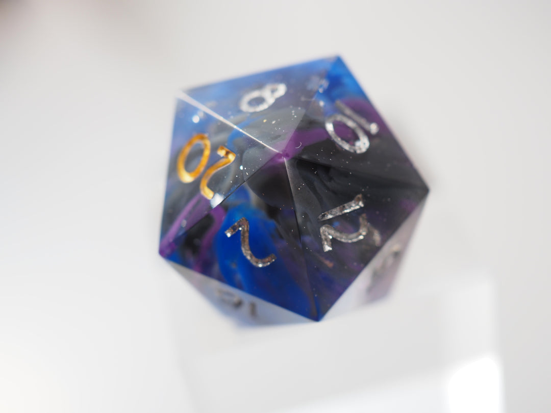 Eine Photographie eines zwanzigseitigen Würfels. Im inneren sind lila, schwarze und blaue Schlieren zu erkennen. Die Zahlen sind in silbern bemalt, außer die 20, welche in Gold bemalt wurde.